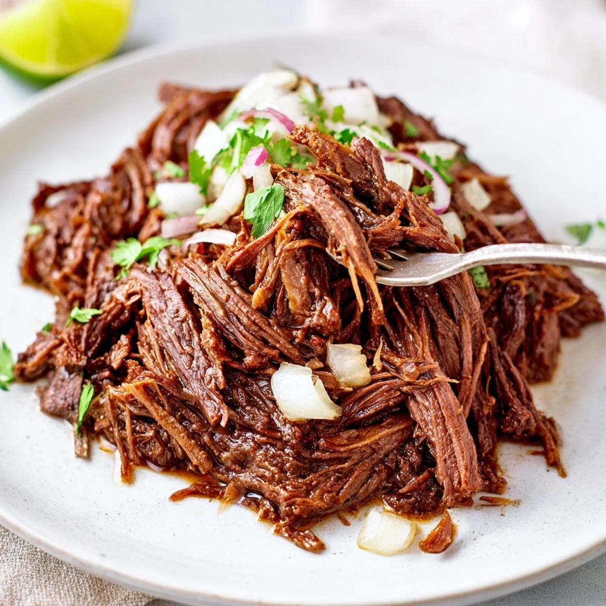 Heaping Slow Cooker Beef Barbacoa bowl with cilantro, lime wedges, juicy shreds