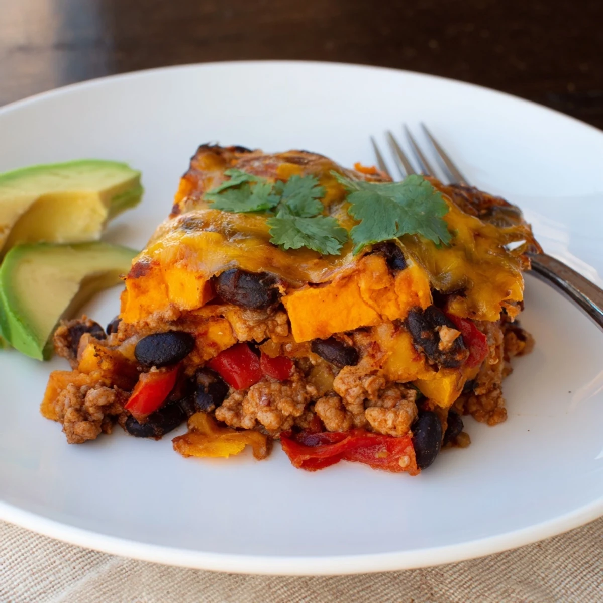 Golden cheesy sweet potato turkey black bean bake garnished with sliced avocado and cilantro