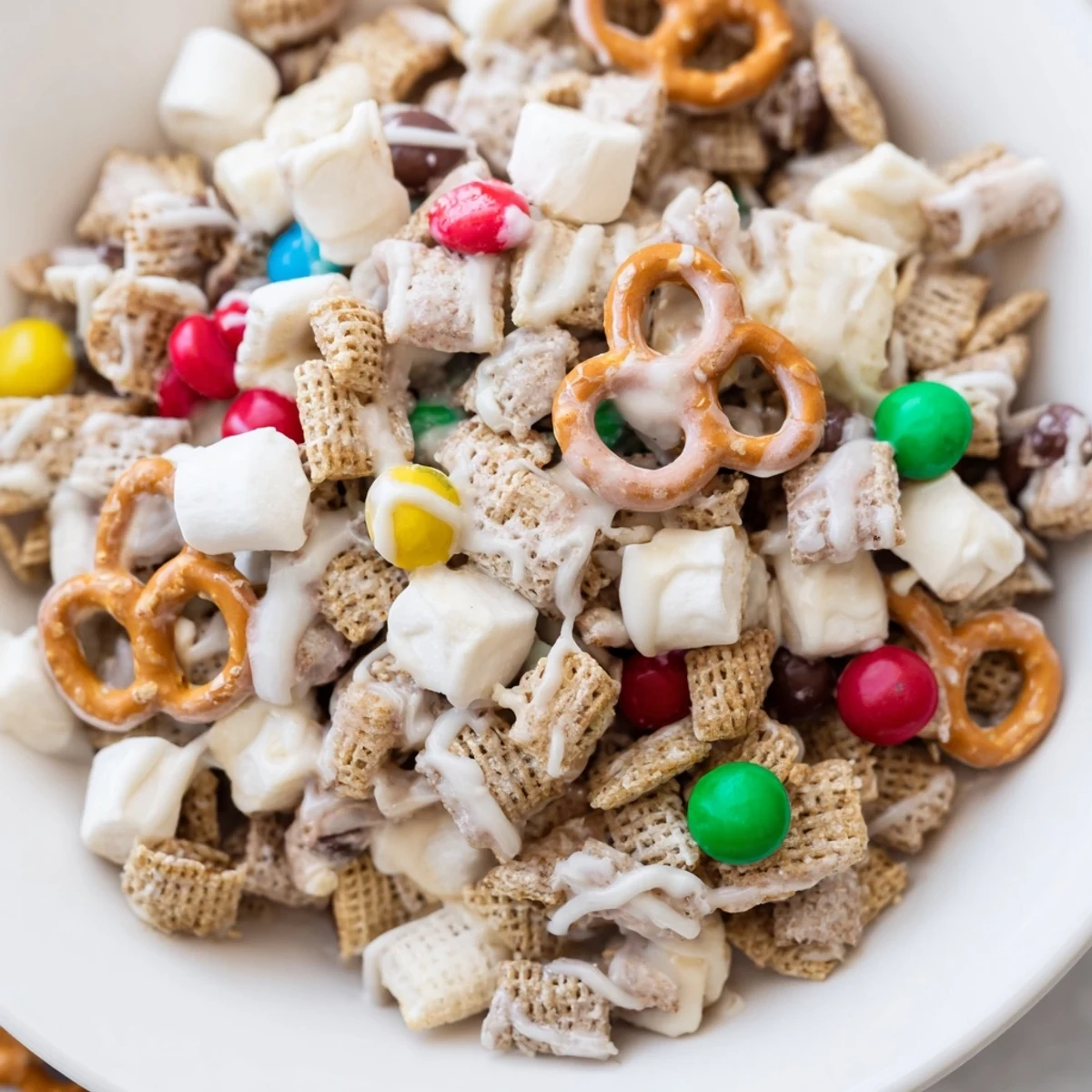 Homemade Reindeer Food holiday treat with melted white chocolate drizzle over cereal, pretzels, and colorful chocolate candies on parchment paper