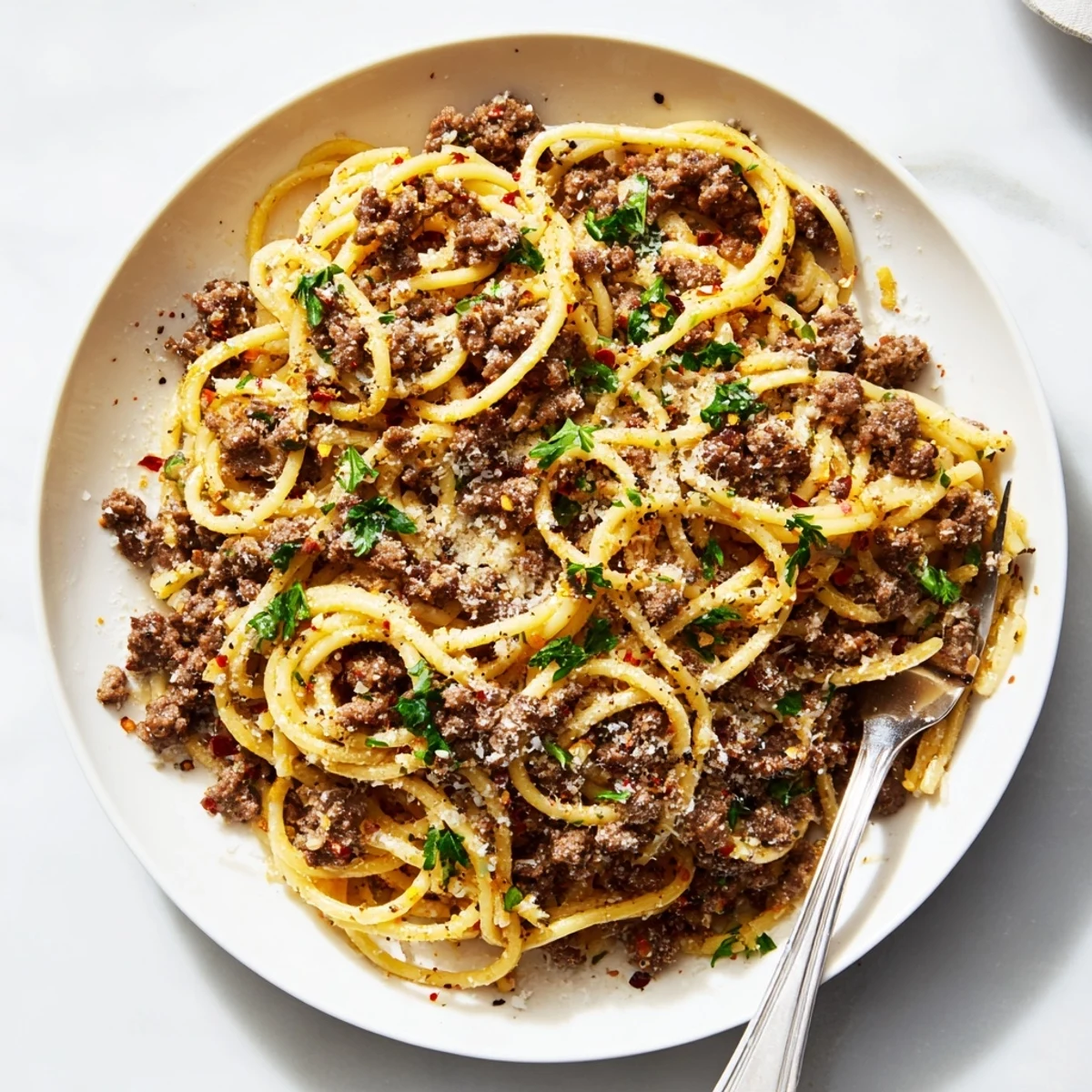 Steaming plate of garlic butter pasta with ground beef garnished with chopped parsley