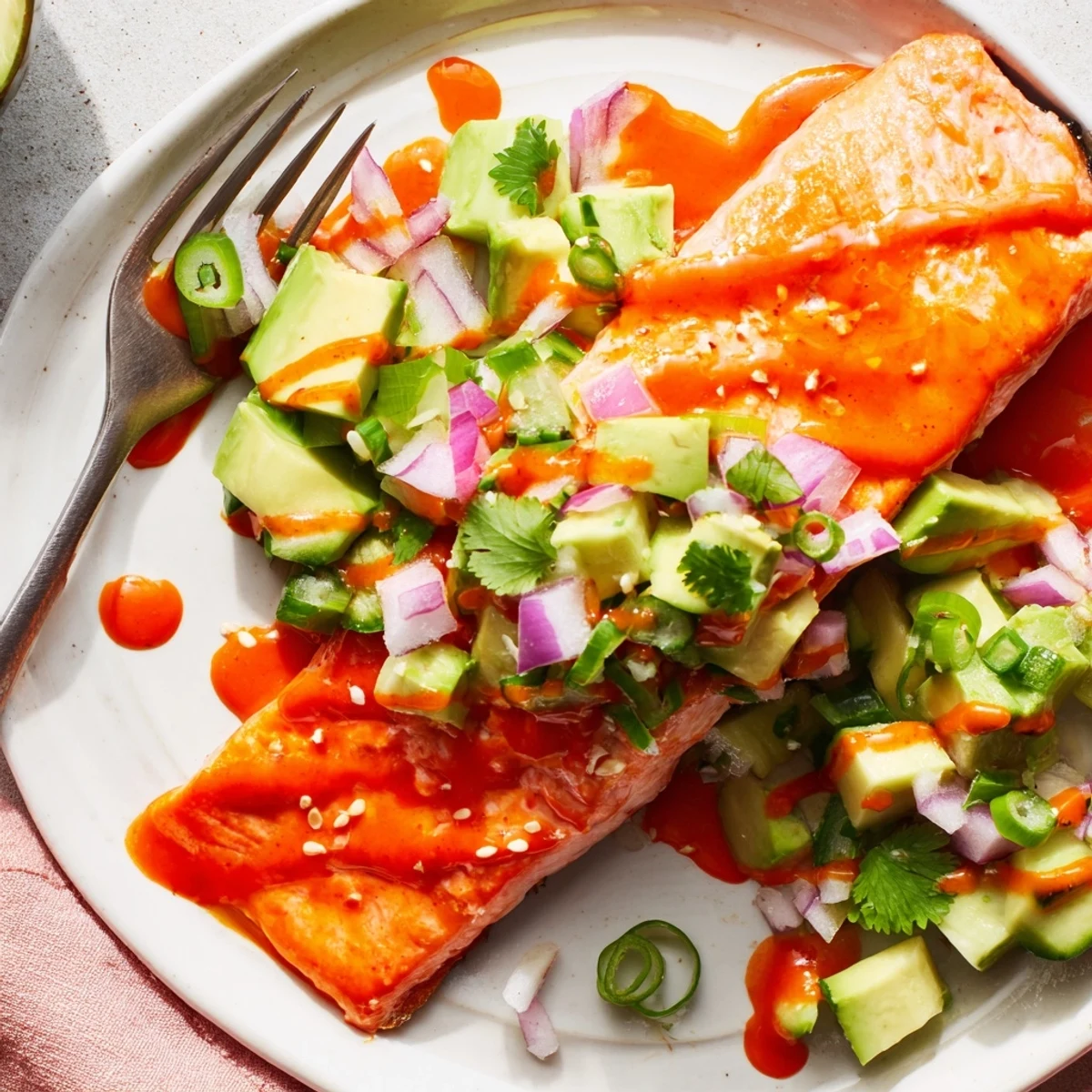 Golden Bang Bang Salmon fillets drizzled with spicy creamy sauce over fresh avocado cucumber salsa.