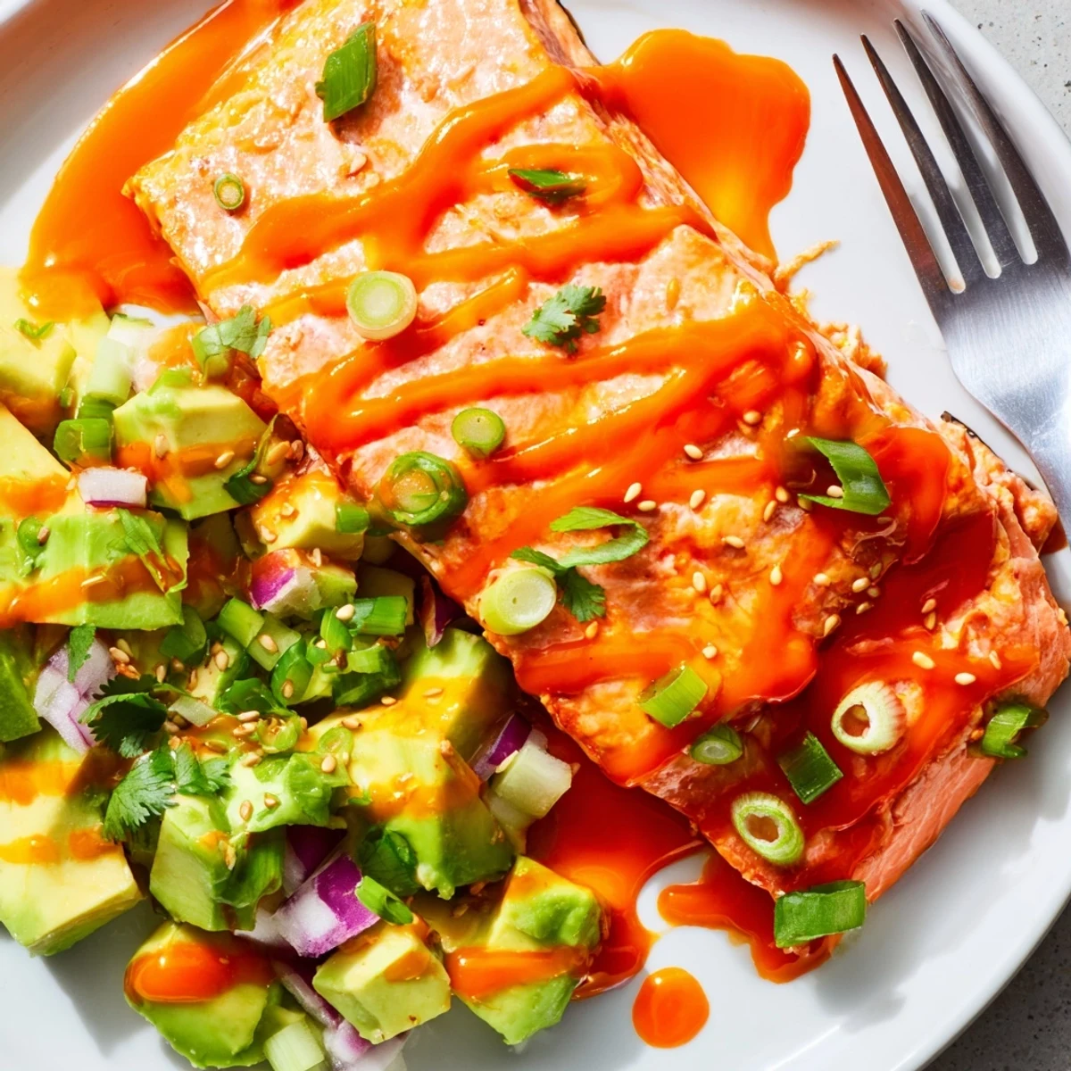 Crispy baked Bang Bang Salmon topped with smooth chili sauce beside vibrant green avocado cucumber salsa.