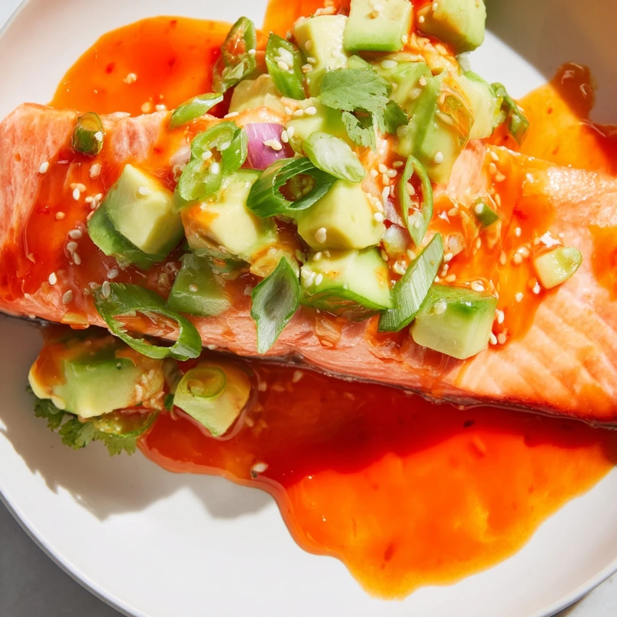 Perfectly glazed Bang Bang Salmon topped with creamy avocado cucumber salsa on a white plate