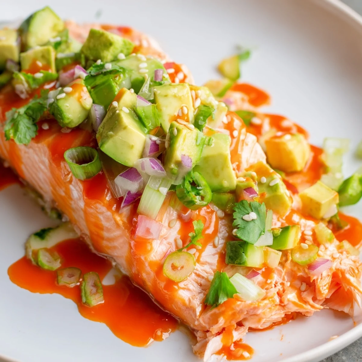 Crispy baked Bang Bang Salmon drizzled with spicy sauce served over cool avocado cucumber salsa