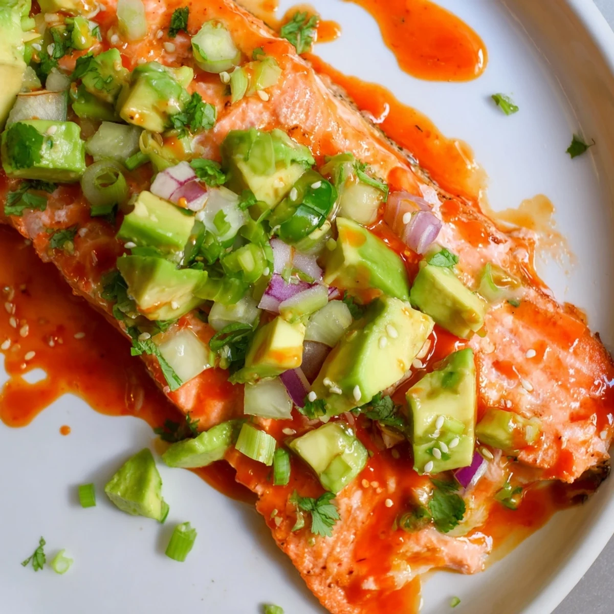 Golden Bang Bang Salmon fillet with vibrant green avocado cucumber salsa and a sprinkle of sesame seeds