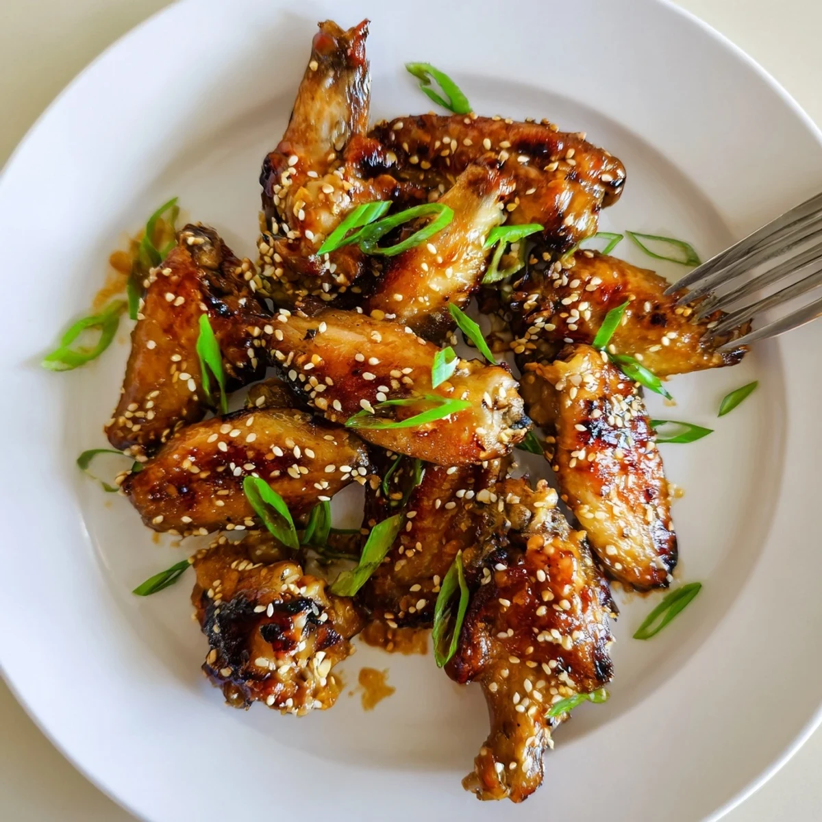Glossy miso honey marinated chicken wings piled on a platter with sesame garnish