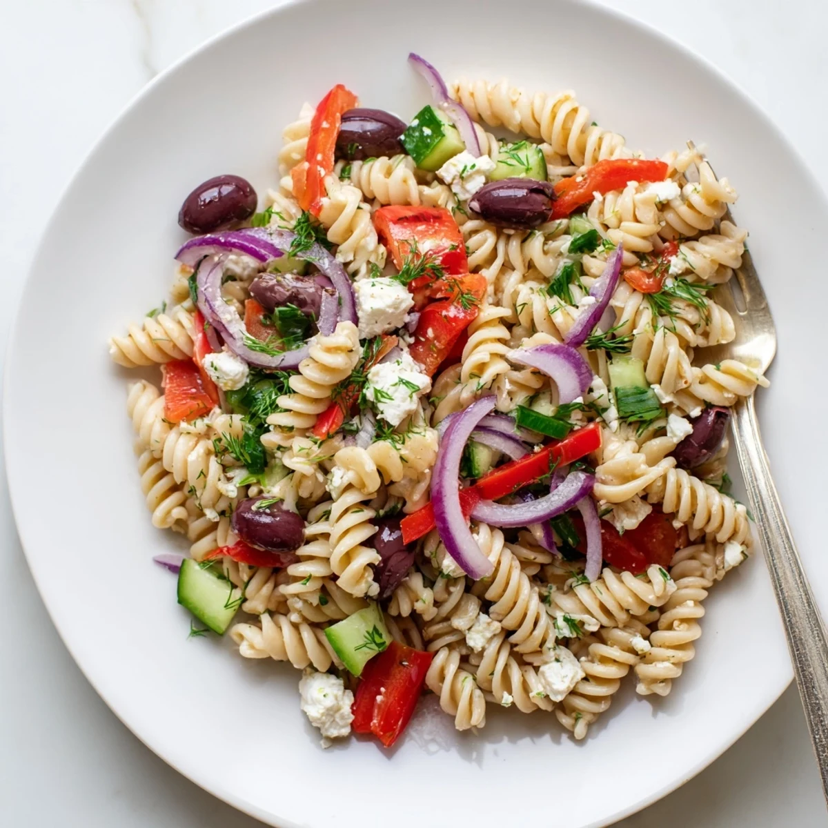 Colorful Greek pasta salad loaded with crunchy vegetables, feta, and olives in a bright bowl