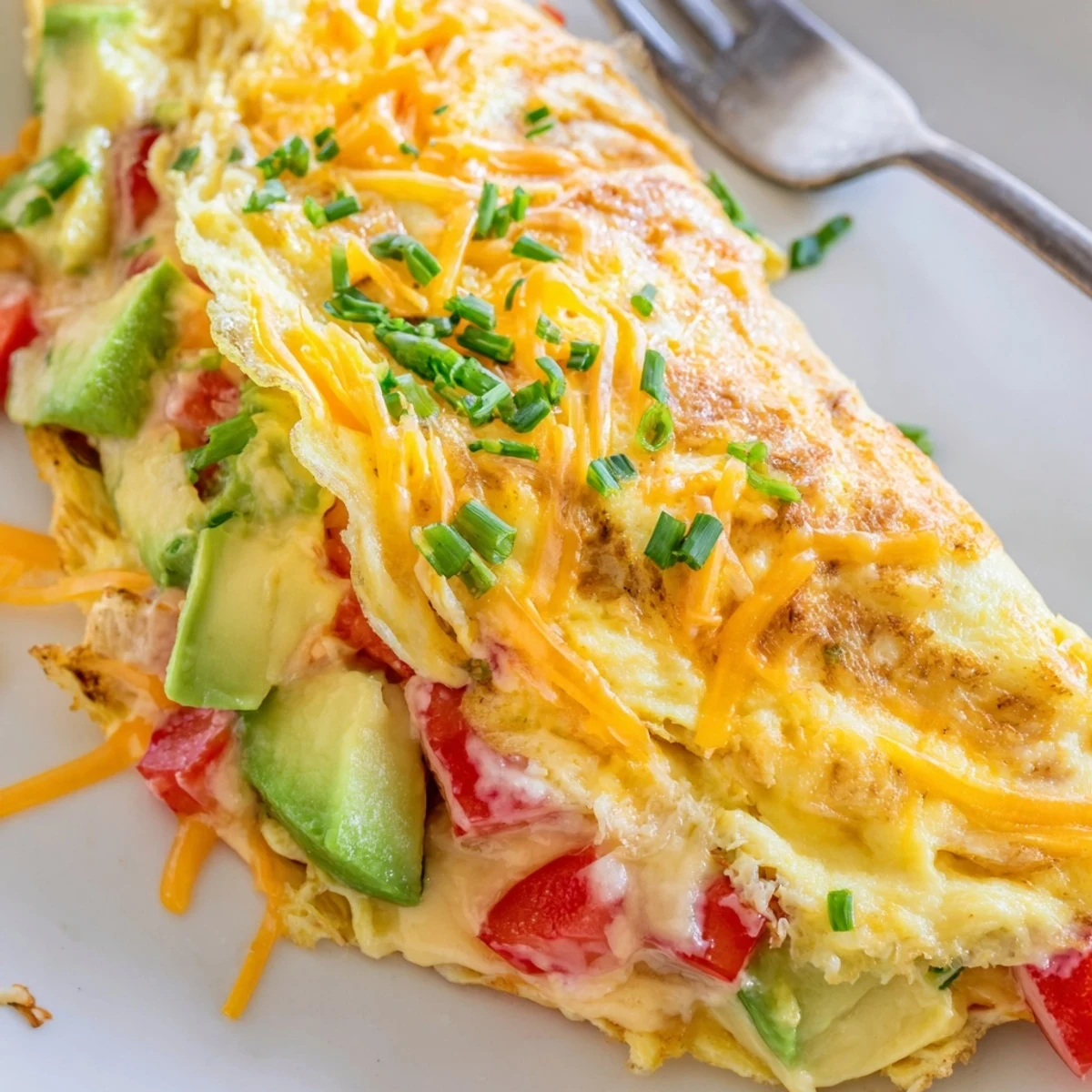 Melted cheddar and ripe avocado spilling from a cheesy tomato omelette