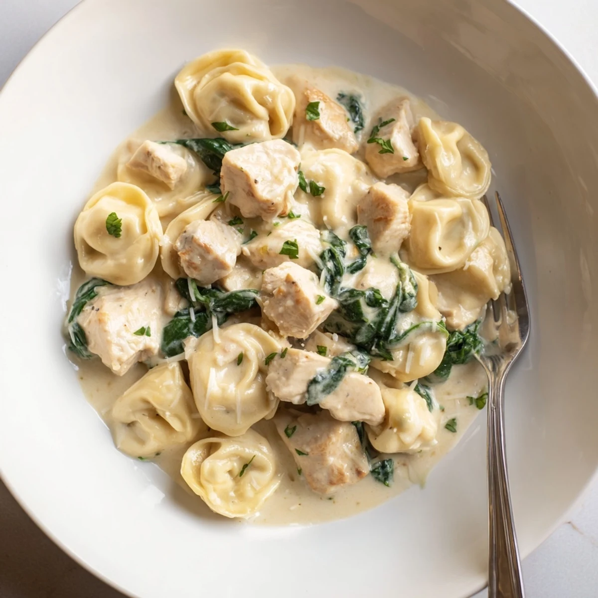 Steaming skillet of creamy garlic chicken tortellini with wilted spinach and melted Parmesan