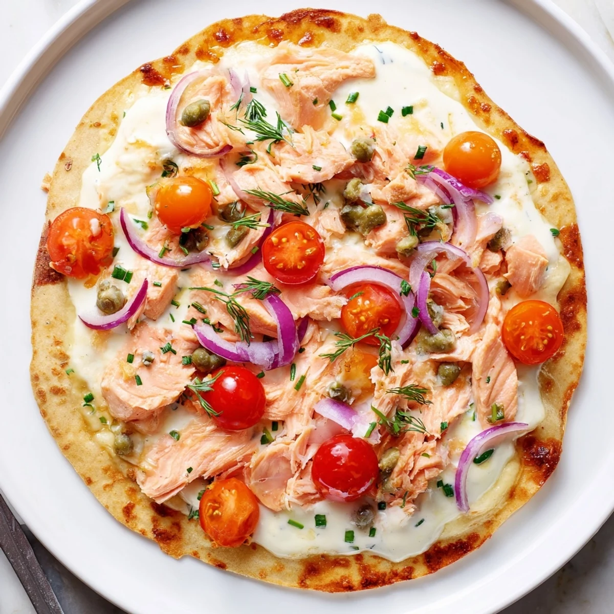 Golden baked salmon tortilla pizza topped with capers, red onion, and bubbling cheese