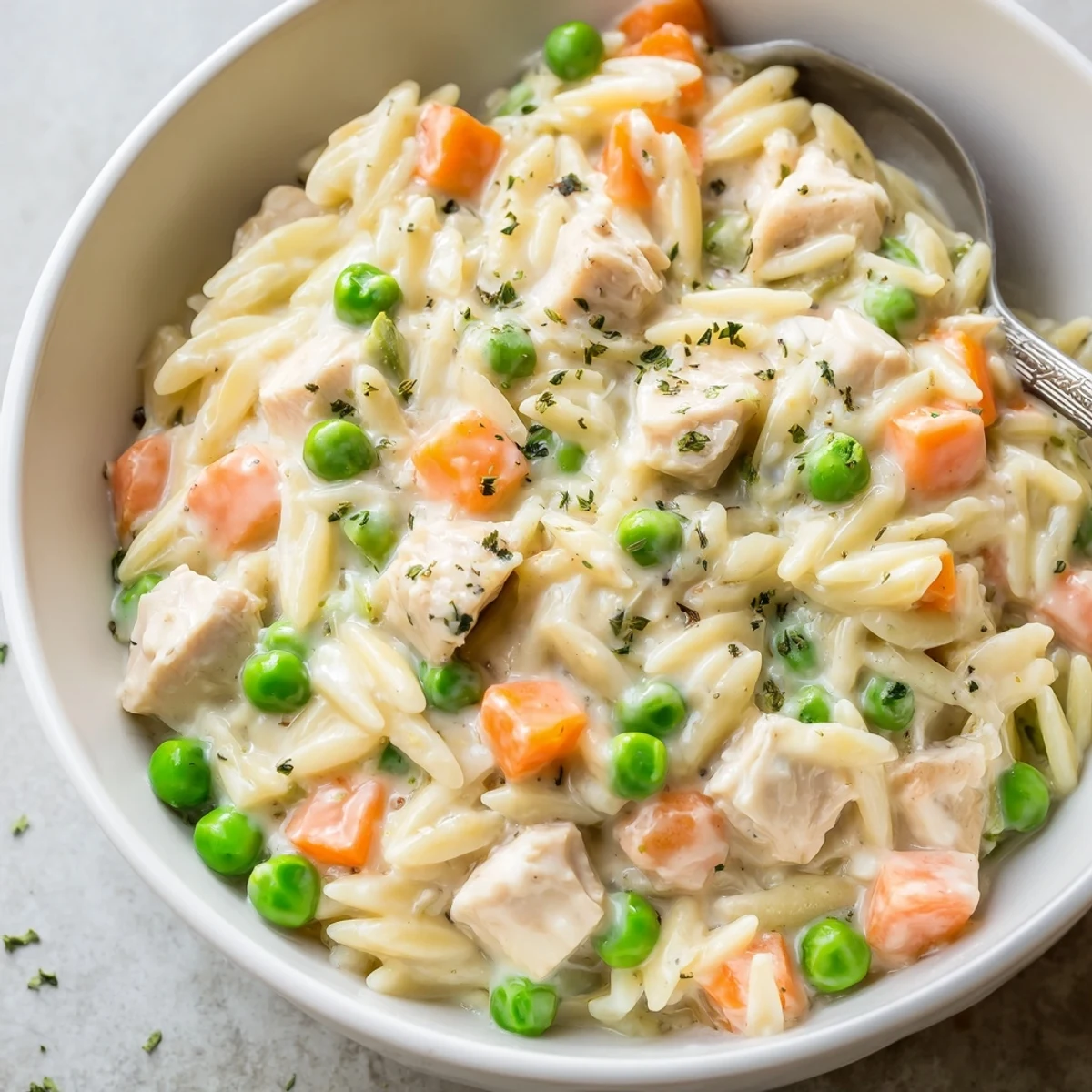 A steaming bowl of Creamy Chicken Pot Pie Orzo loaded with tender vegetables.
