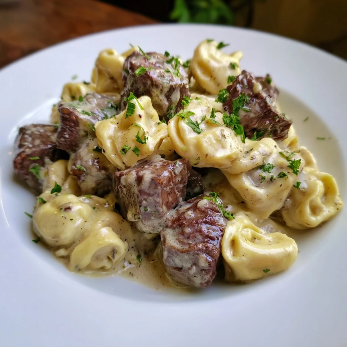Creamy garlic steak tortellini plated in a white bowl, garnished with fresh parsley.