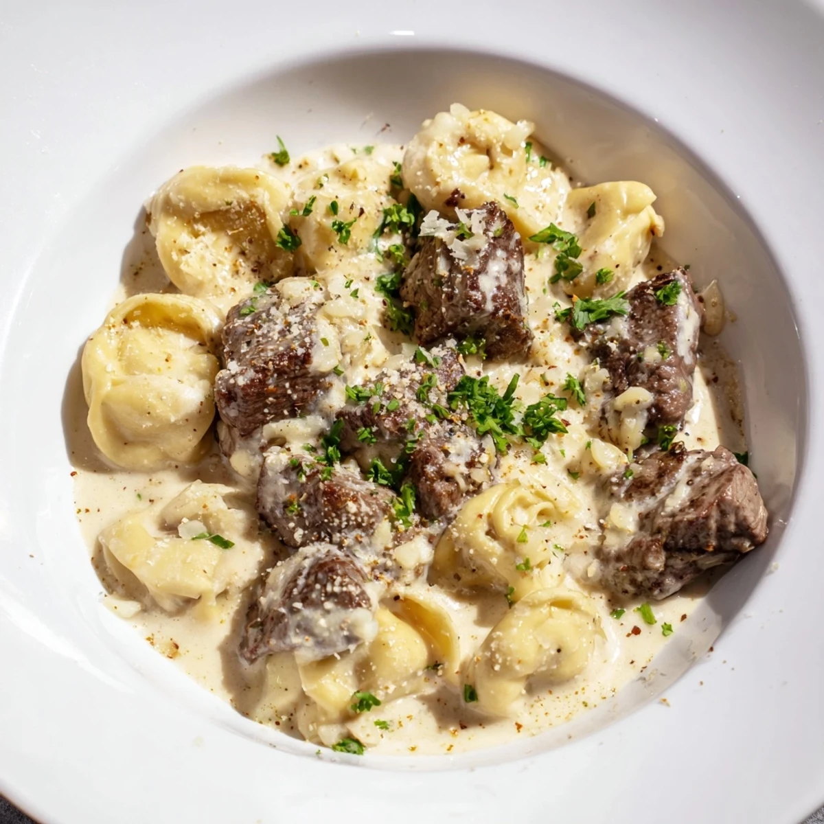 Steaming hot garlic steak tortellini served on a dark plate with grated Parmesan.