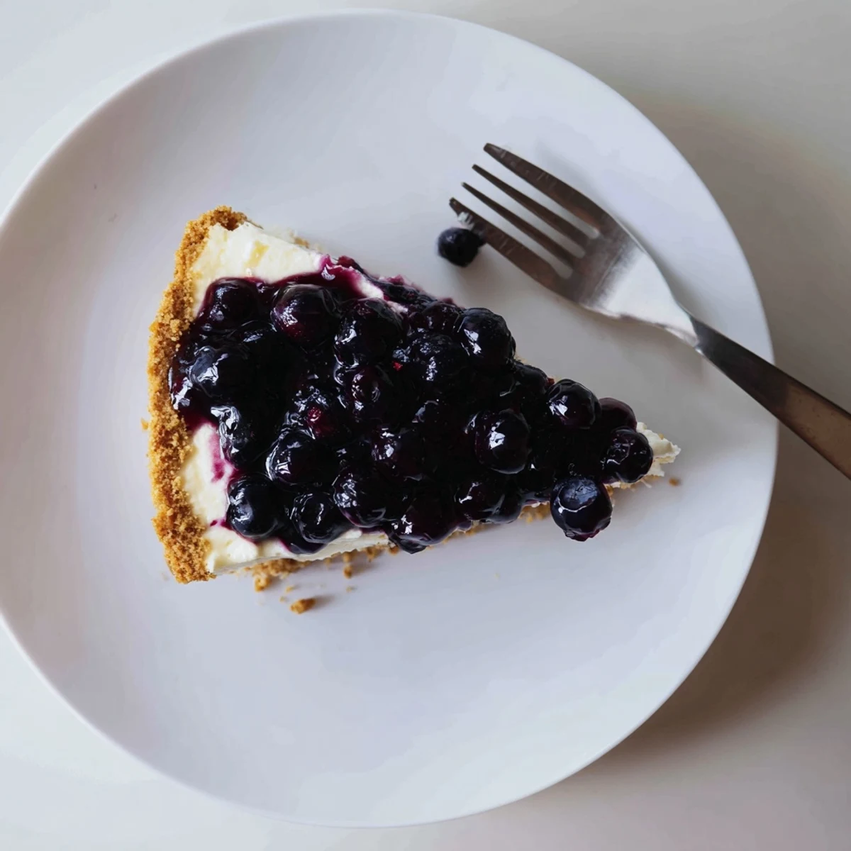Creamy blueberry cheesecake slice topped with glossy purple compote and fresh berries.
