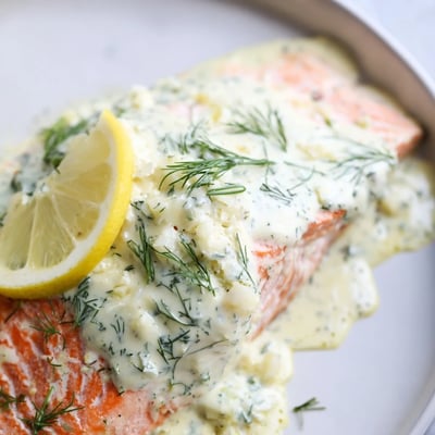 Tender, oven-baked salmon topped with fresh dill sauce and lemon slices, plated alongside steamed asparagus.