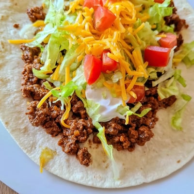 A close-up of juicy ground beef tacos with fresh tomatoes and cilantro on a rustic table.