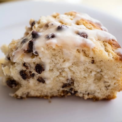 Golden brown Chocolate Chip Scones with Sweet Vanilla Glaze on a white plate, paired with a steaming coffee.