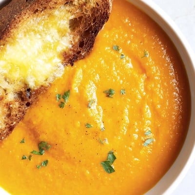 A close-up of velvety orange carrot soup with a swirl of cream and a sprinkle of fresh coriander.
