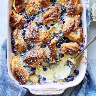 Golden-brown Blueberry Cream Cheese Croissant Casserole baked in a dish, ready to serve with a dusting of powdered sugar.