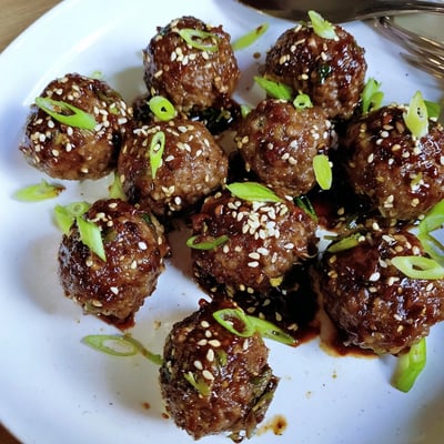 Baked Firecracker Meatballs steaming on a platter, garnished with sliced spring onions.  